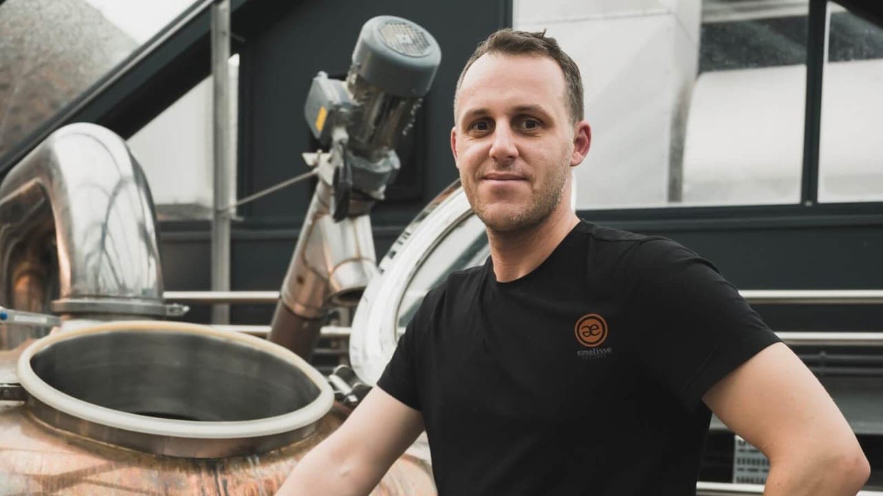 Brouwer van Emelisse in een Emelisse-shirt naast de koperen brouwketel